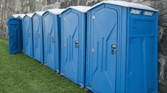 Row of blue portable toilets lined up on grass against a stone wall for event sanitation in Reno, NV
