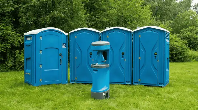 Four blue portable toilets and a matching hand washing station on grass near trees, a common sight at local outdoor events in Reno, NV