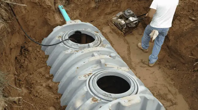 Septic tank installation showing a technician compacting soil around a new poly septic tank in an excavation pit in Reno, NV